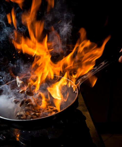 Side view mushroom frying with stove and fire and human hand in pan on black background